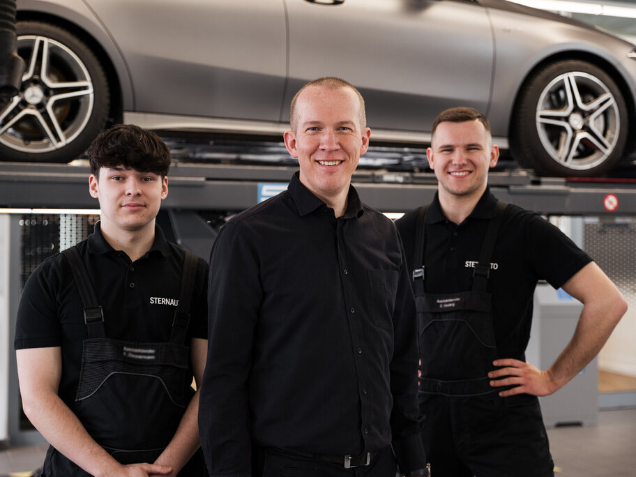 3 Mechaniker stehen vor Hebebühne mit Auto