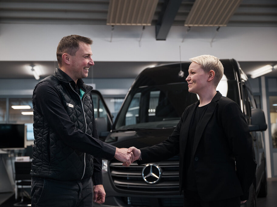 Handschlag zwischen Serviceberater und Kundin vor Mercedes-Benz Transporter